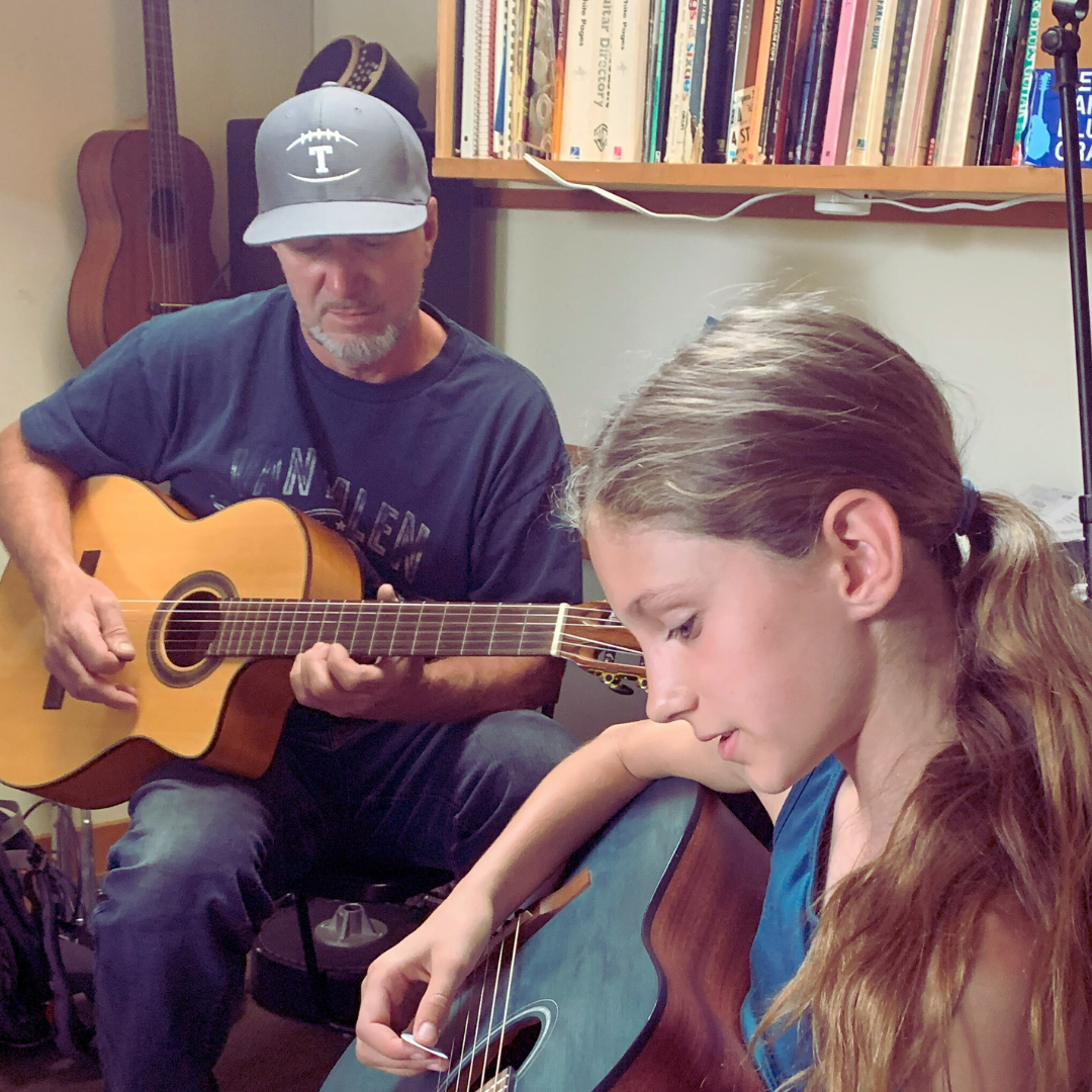 Instructor and student playing guitars together during lesson