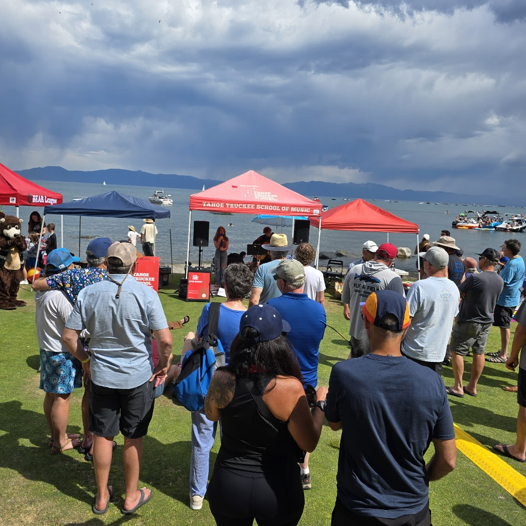 Crowd watching TTSM performance at lakeside with mountains and dramatic clouds