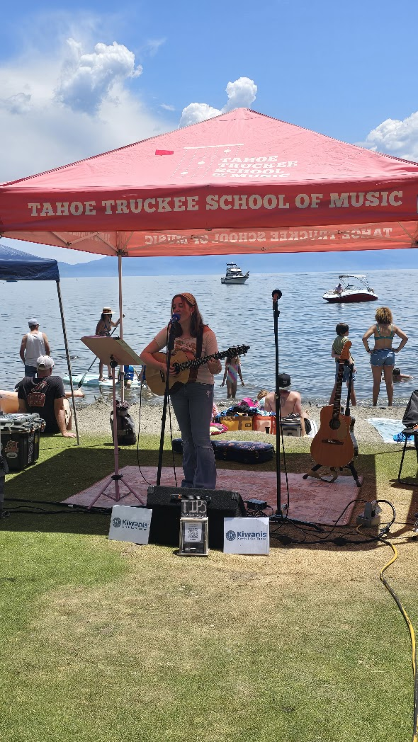 Performer playing ukulele under TTSM tent on the beach with Lake Tahoe behind